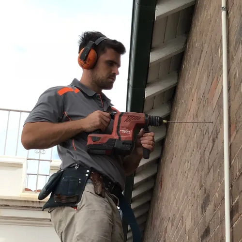 Buildfix technician drilling helical wall ties through outer brick leaf into inner leaf