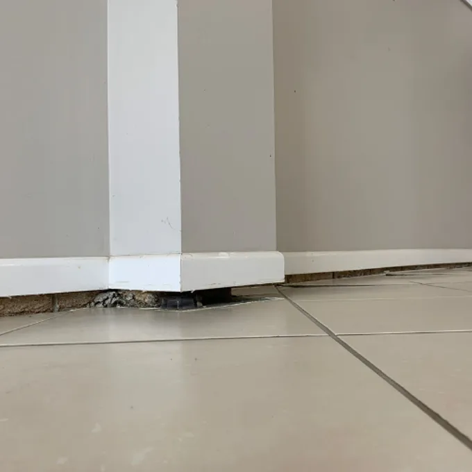 Tiled floor dropping away from skirting board with exposed gap at base