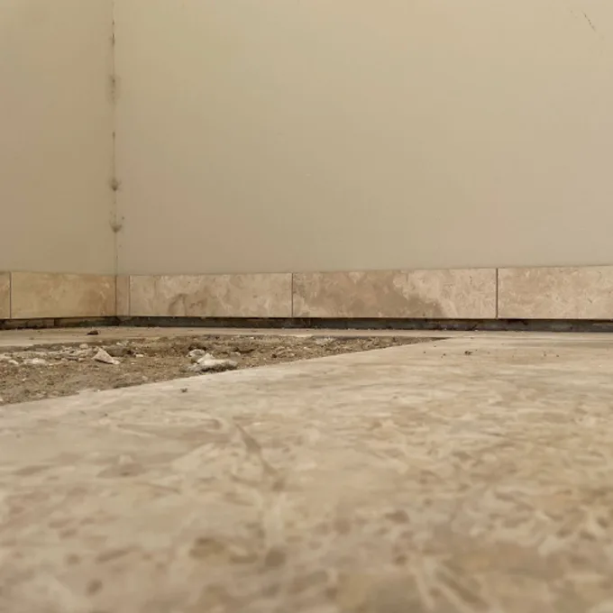 Floor tiles lifting with visible gap between tile edge and skirting