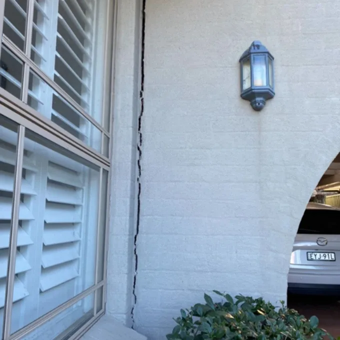 Rendered wall separating with wide vertical crack beside window